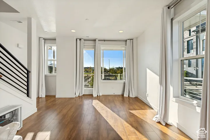 Open-concept interior featuring wood-finish flooring, recessed lighting, expansive windows, and a staircase with a metal railing