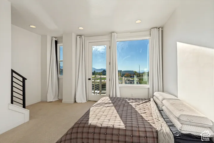 Carpeted room featuring floor-to-ceiling windows, a glass-panel exterior door, recessed ceiling lighting, and a metal-railing staircase