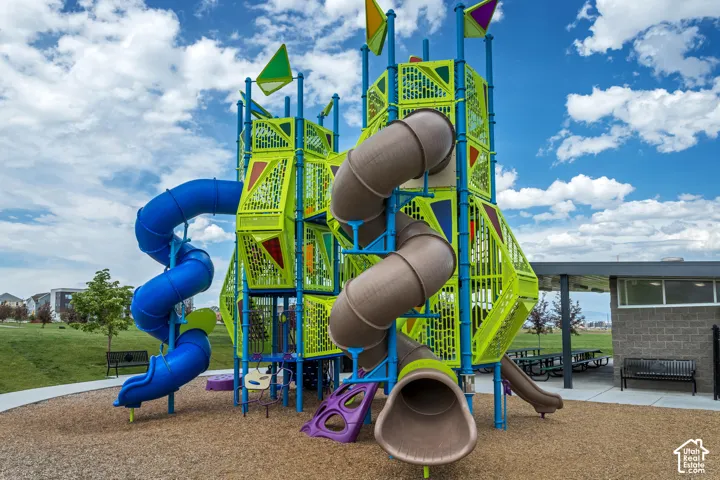 Multi-level playground structure featuring dual spiral slides, a covered outdoor pavilion with concrete flooring, and metal seating benches