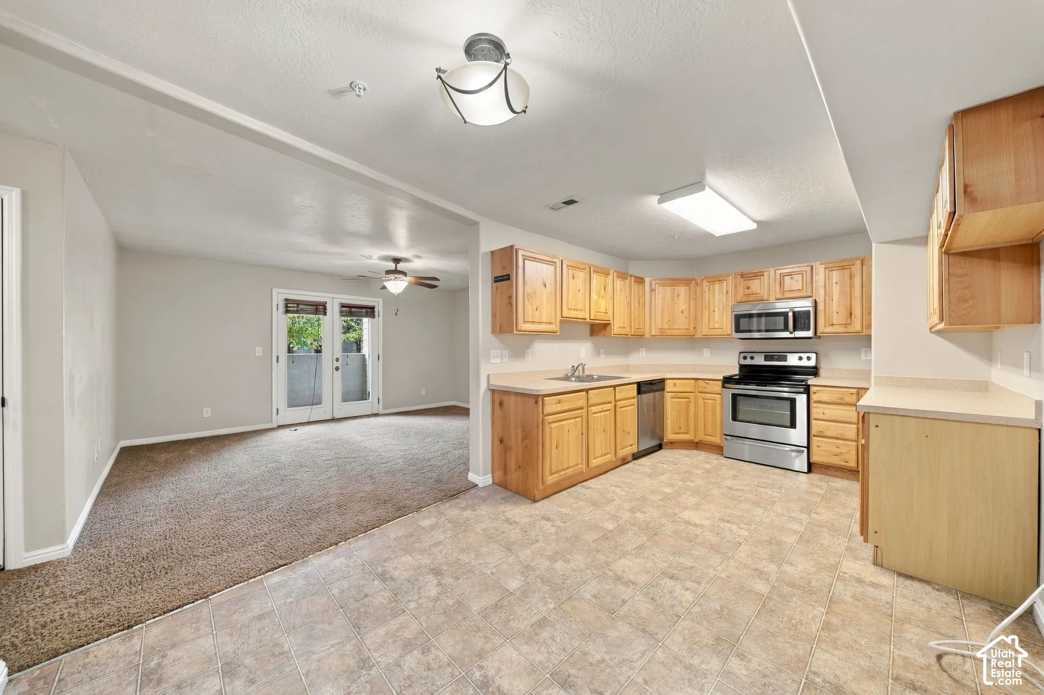 Kitchen featuring natural wood cabinetry, laminate countertops, and stainless steel appliances, including a built-in microwave and range, paired with durable tile flooring
