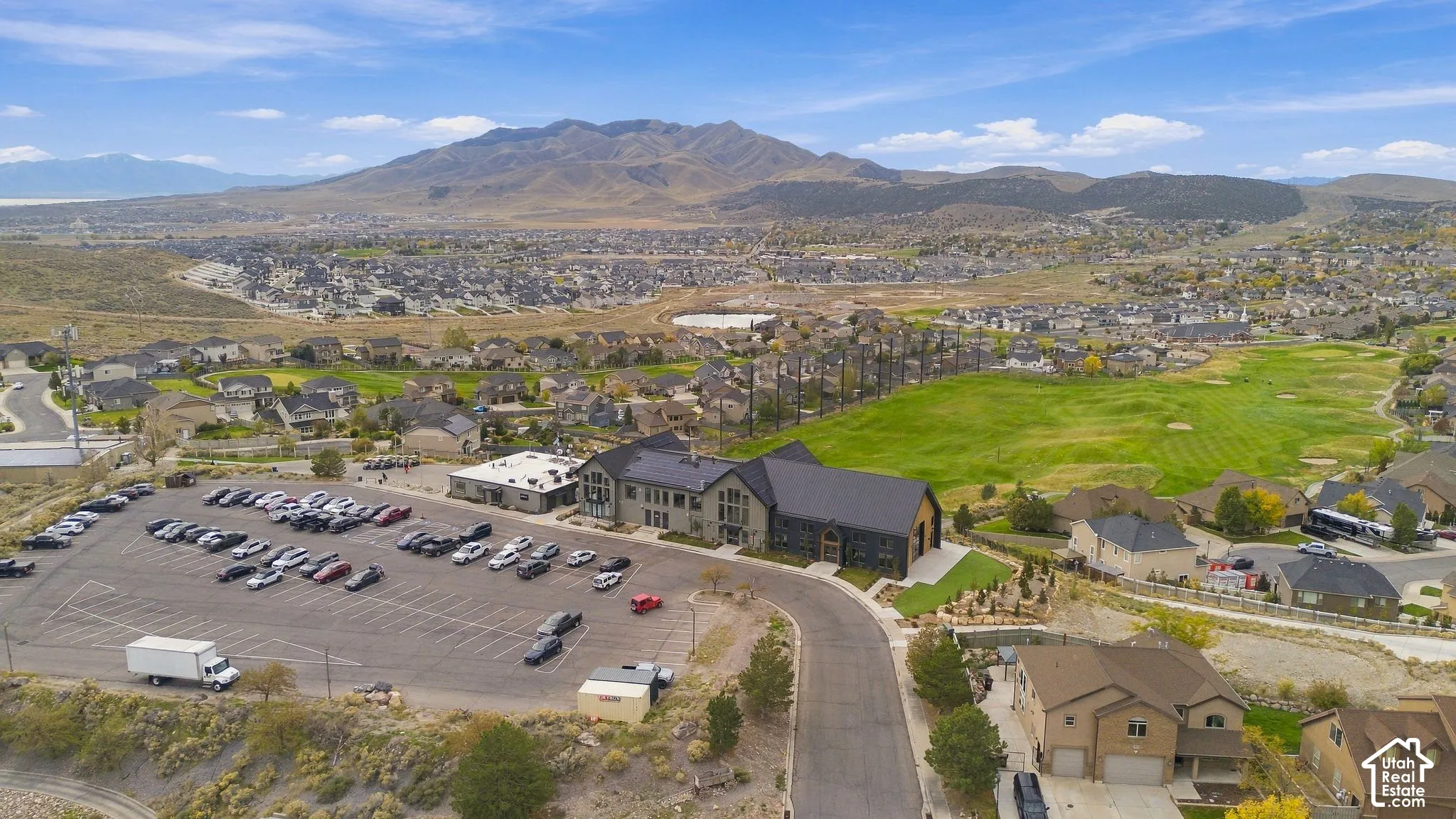 Aerial perspective of a multi-structure property featuring dark metal roofing, mountain backdrops, and expansive paved parking