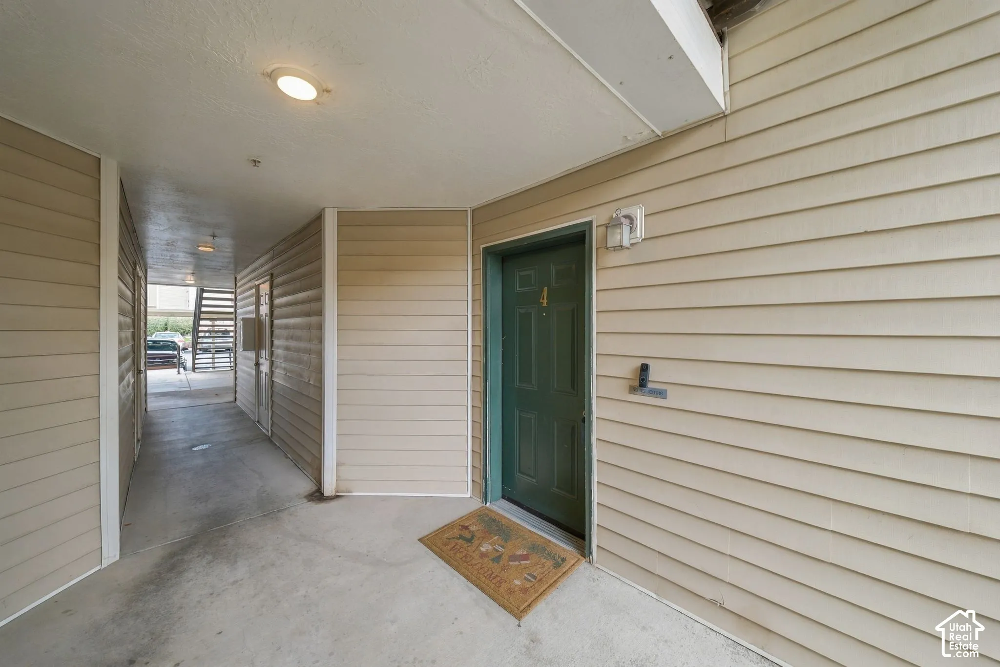 Exterior entryway featuring horizontal siding, a solid-paneled door, concrete flooring, and wall-mounted lighting