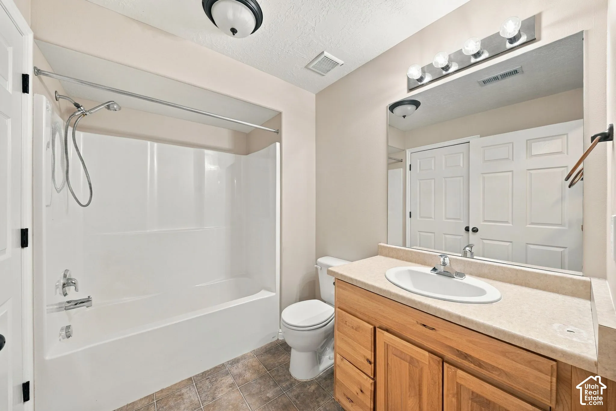 Bathroom featuring a wood-finish vanity with a molded countertop and integrated sink, a full-width vanity mirror, a tub-shower combination with a surround, and tile flooring