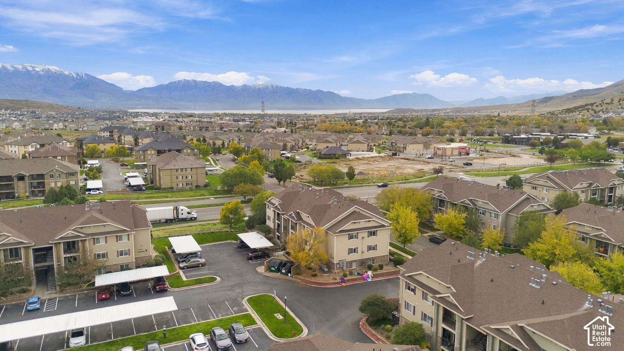 Aerial perspective featuring multi-story residential structures, covered parking carports, paved surface lots, and a backdrop of mountain ranges