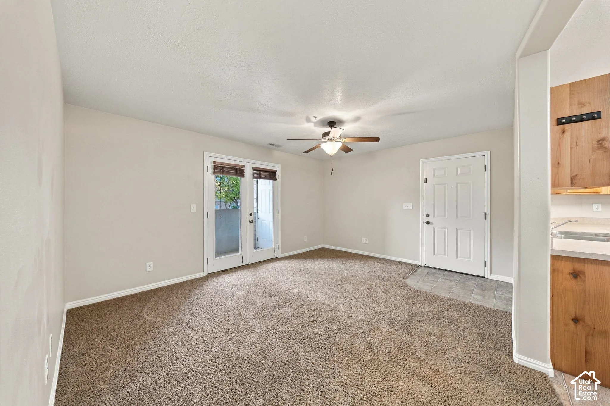 Living area featuring neutral carpeting, a central ceiling fan with integrated lighting, glass-paneled French doors, and tile entryway flooring