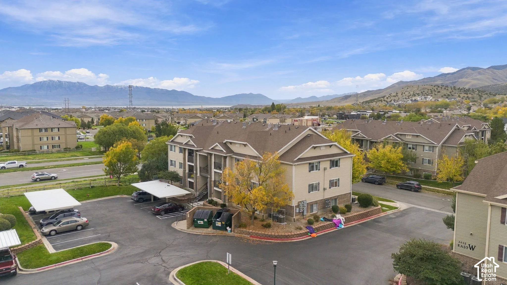 Multi-story residential complex featuring neutral-tone siding, gabled rooflines, stone-veneer accents, covered parking structures, and mountain backdrops