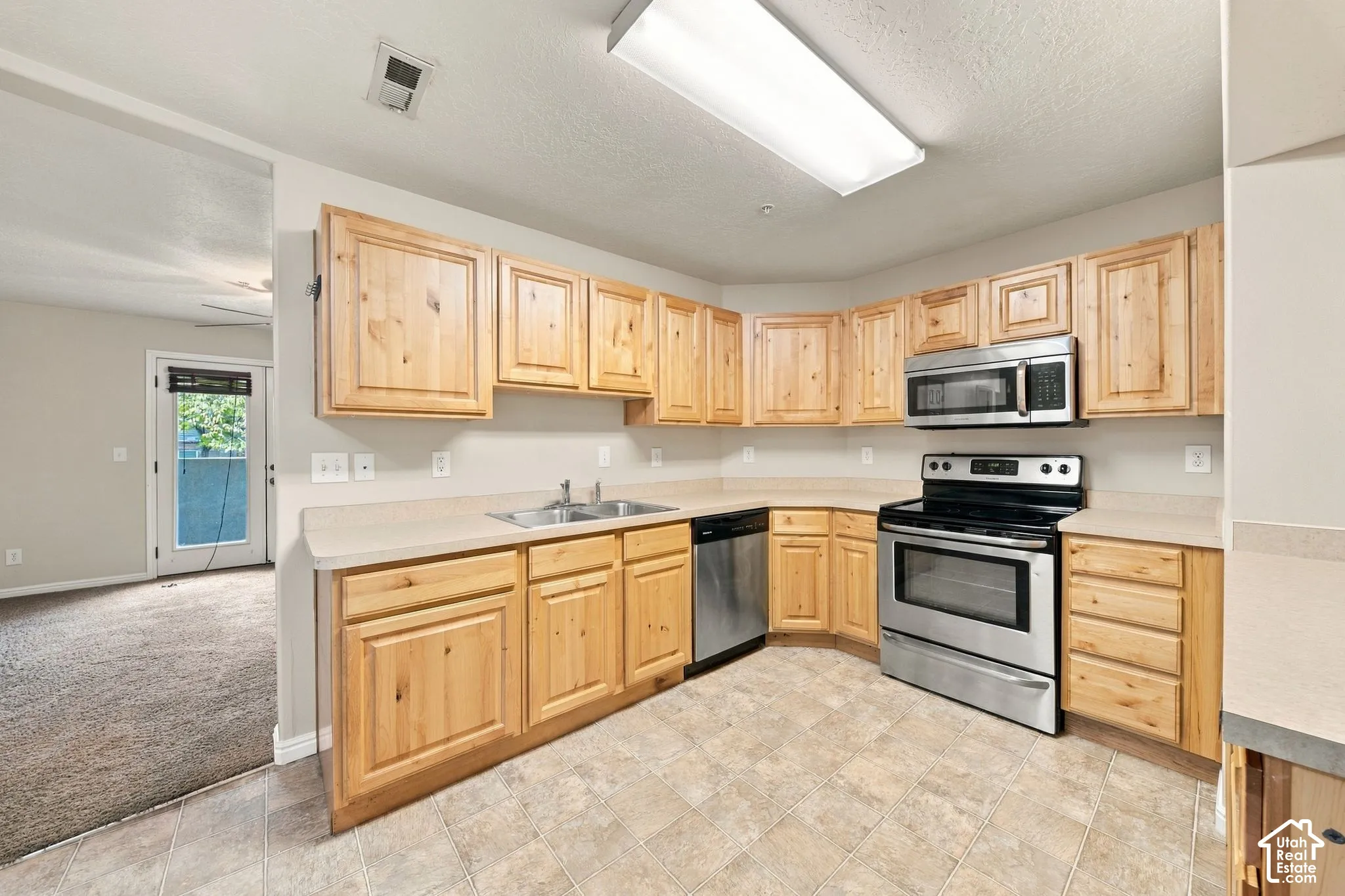 Kitchen featuring natural finish wood cabinetry, stainless steel oven, stainless steel microwave, integrated dishwasher, and solid surface countertops
