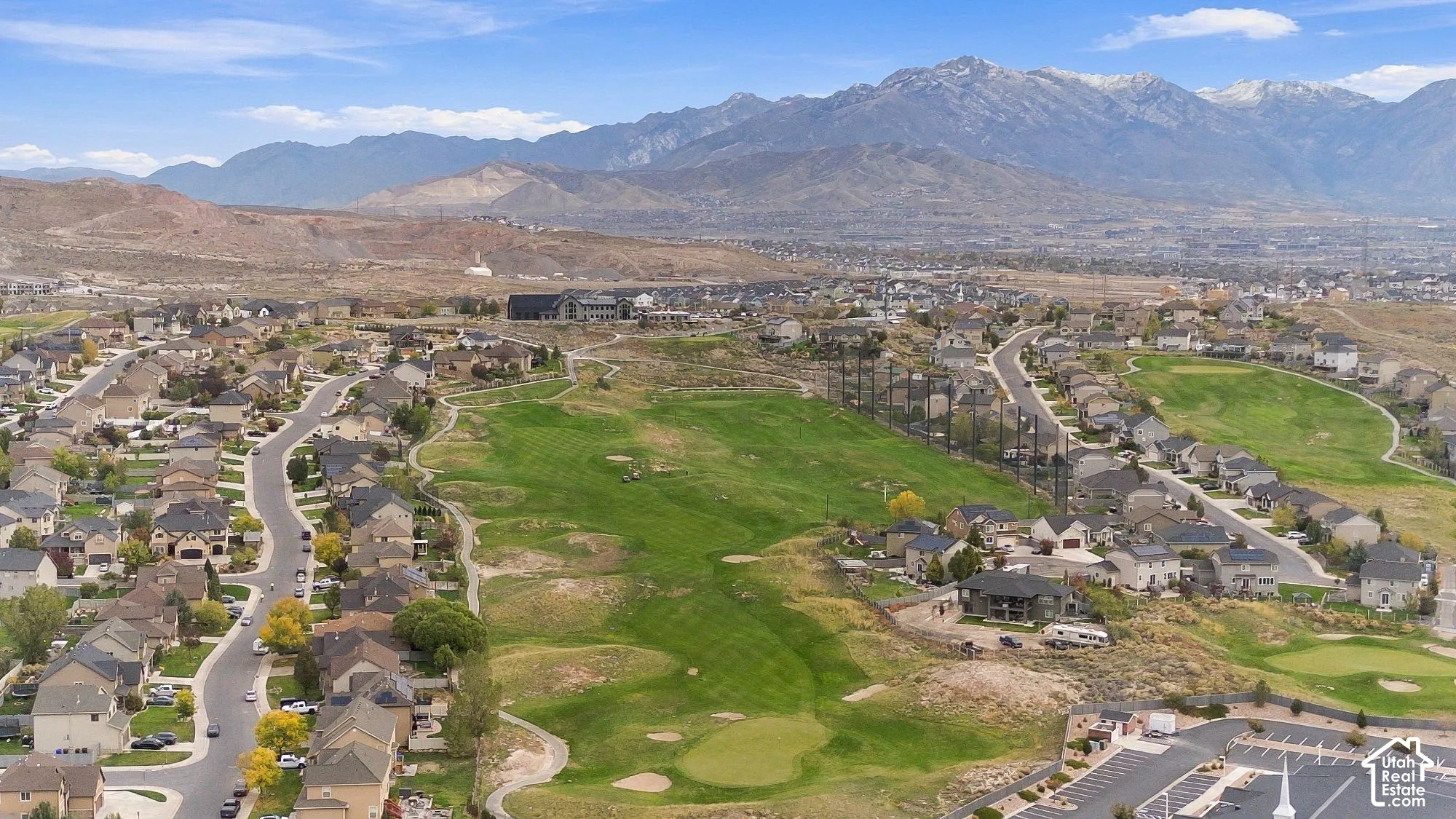 Aerial perspective of a residential neighborhood featuring golf course fairways, expansive mountain range backdrop, and paved cul-de-sac streets