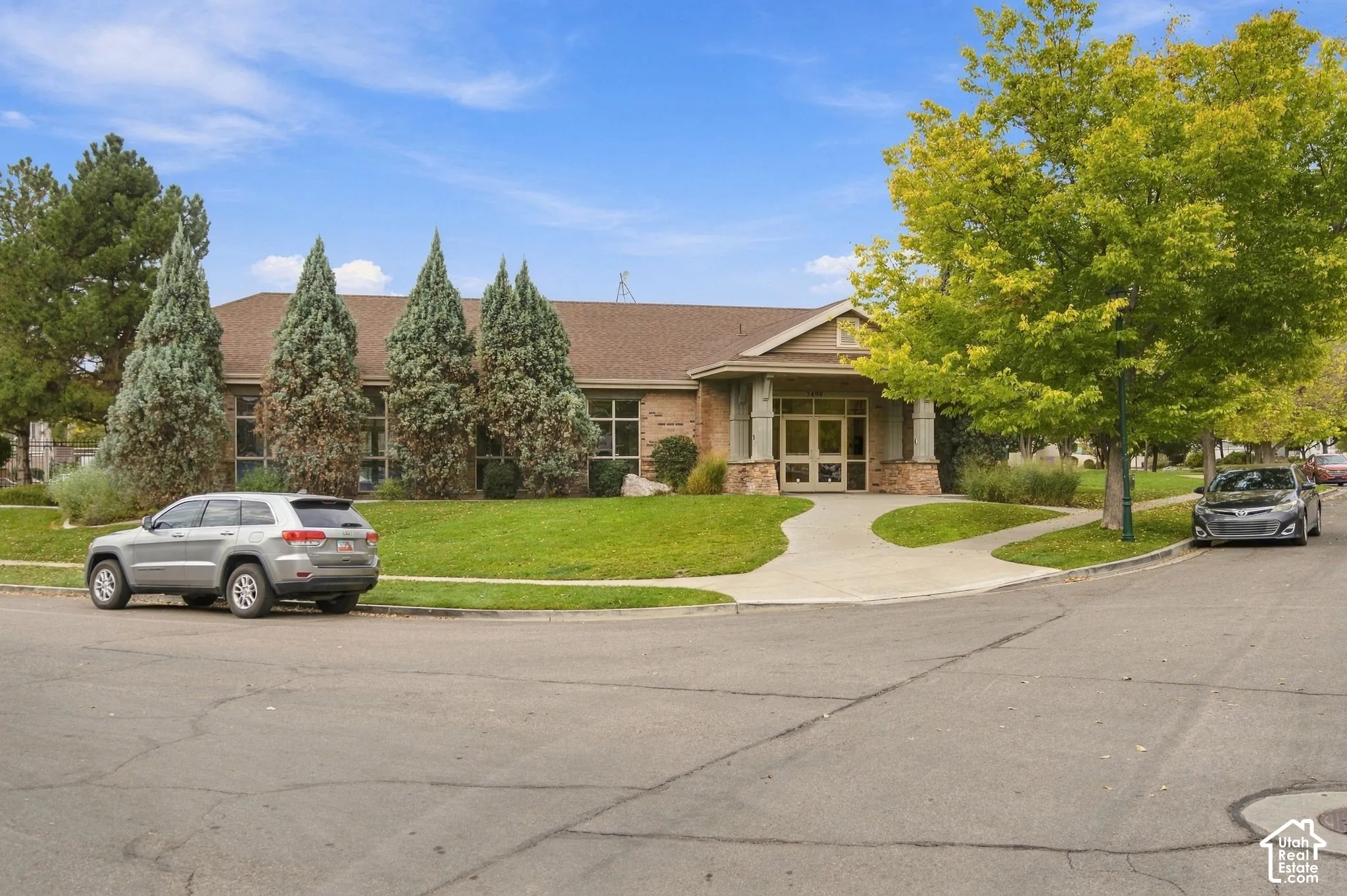 Single-story exterior featuring a brick and siding facade, covered entryway with stone columns, and multi-pane glass entrance doors, set upon a corner lot with mature landscaping