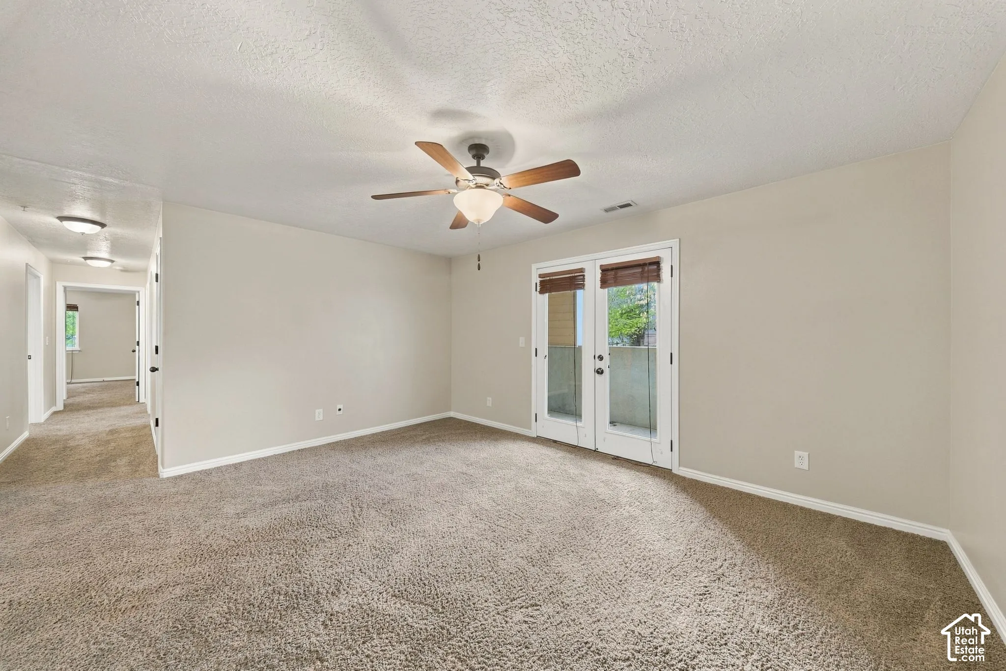 Neutral-toned interior space featuring neutral wall-to-wall carpeting, glass-paned double doors, and a ceiling-mounted light fixture with an integrated fan