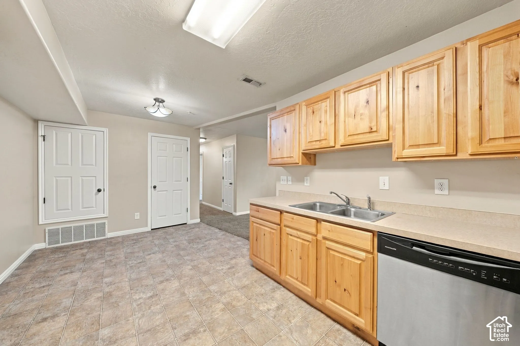 Natural wood cabinetry, stainless steel dishwasher, dual-basin stainless steel sink, and solid-surface countertop