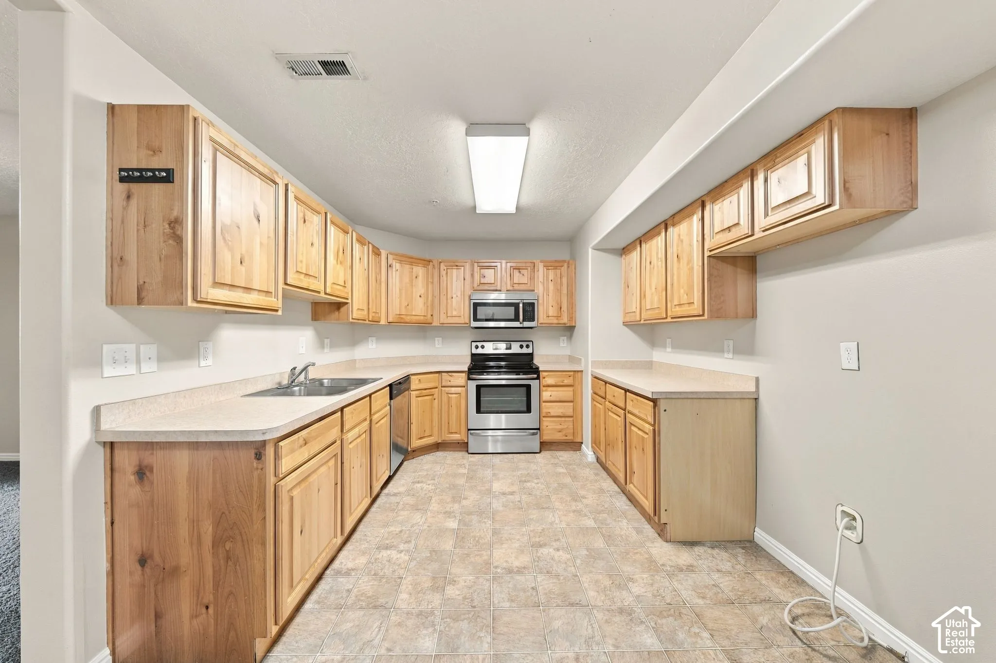 Kitchen featuring light wood cabinetry, neutral laminate countertops, and stainless steel range and microwave