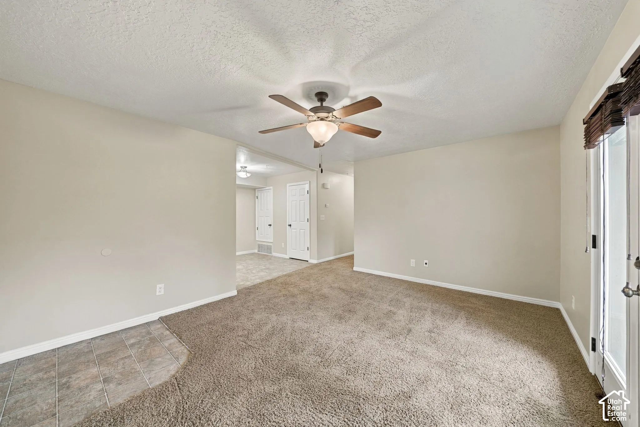 Neutral-toned interior featuring wall-to-wall carpeting, tile flooring, a central ceiling fan with integrated lighting, and a glass-paneled exterior door