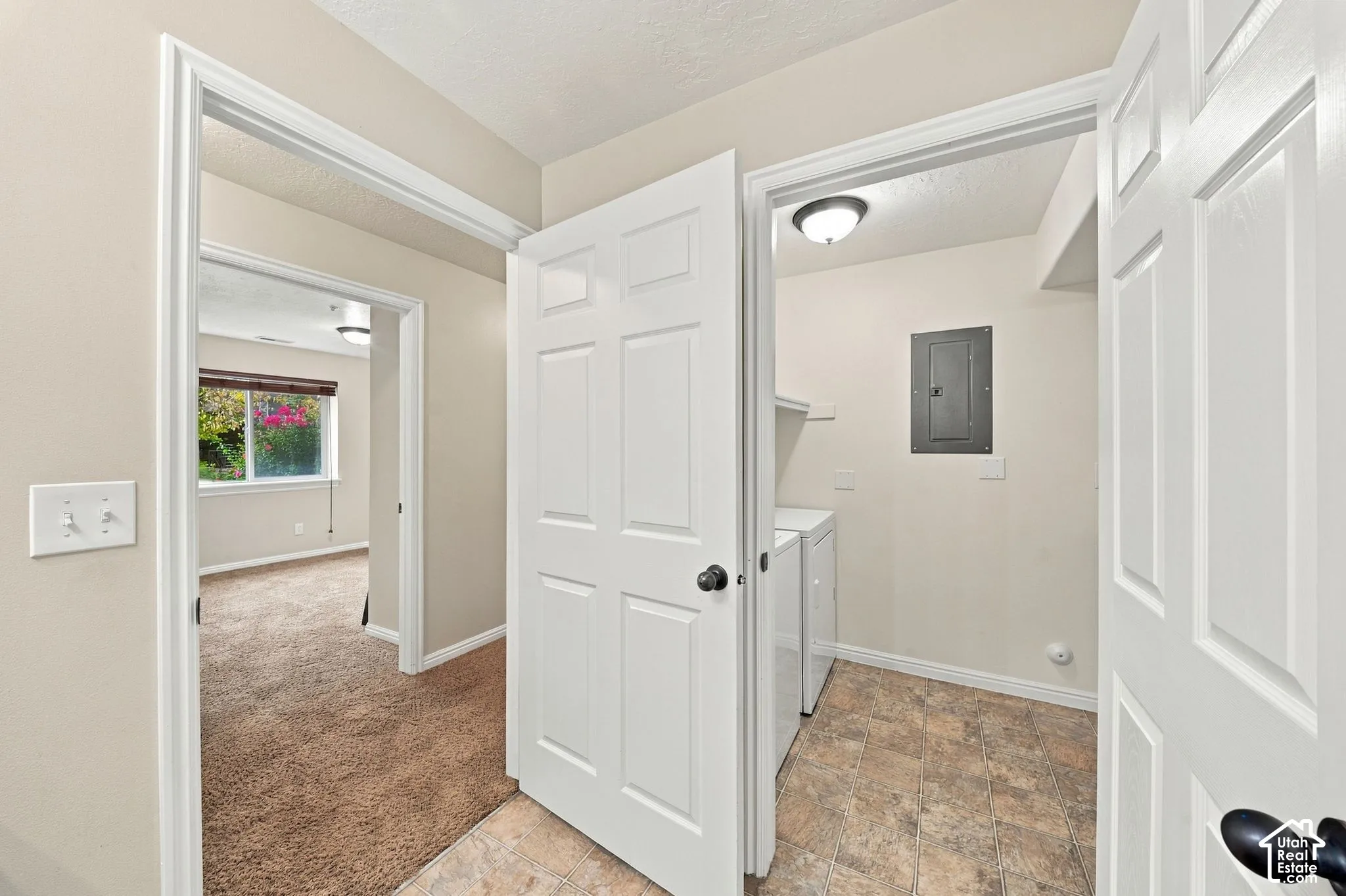 Laundry area featuring tile flooring, neutral wall paint, and overhead lighting, with interior paneled doors and carpeted flooring in the secondary room