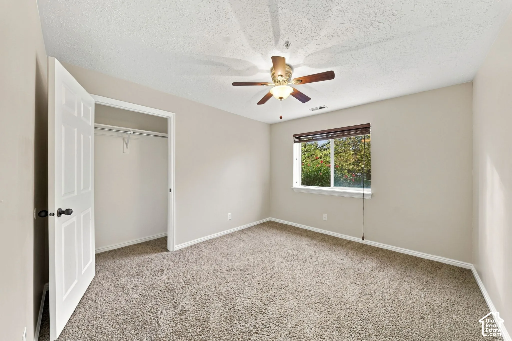Neutral-toned interior featuring wall-to-wall carpeting, a ceiling fan with integrated lighting, a single-panel interior door, and a reach-in closet with built-in shelving