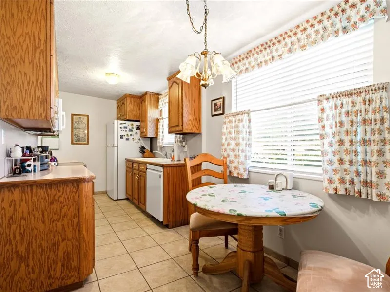 Kitchen featuring wood cabinetry, tile flooring, built-in dishwasher, white appliances, and a multi-arm hanging light fixture