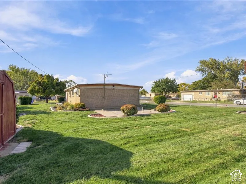 Expansive backyard featuring a large grass lawn, brick exterior, concrete patio, and mature trees