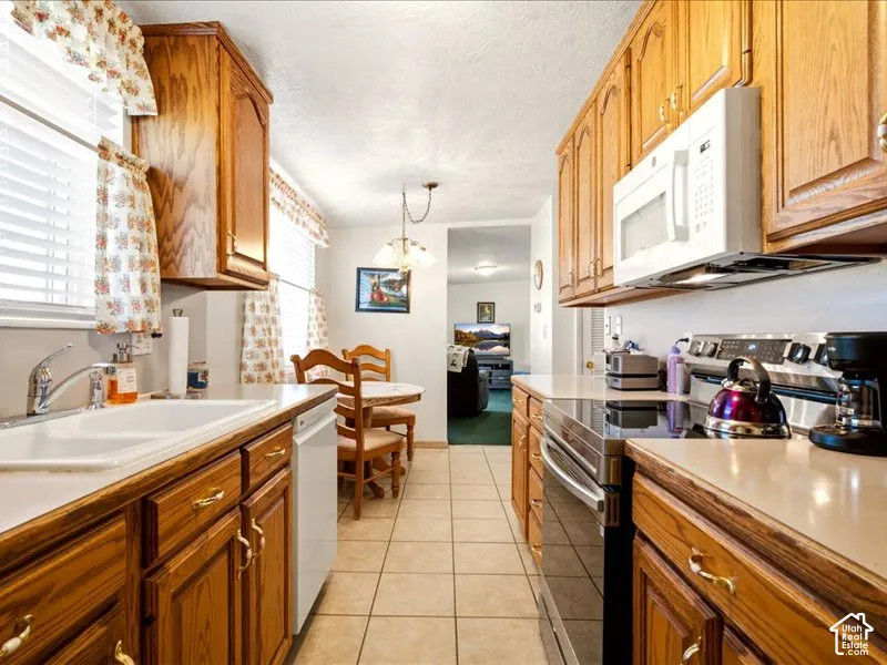 Kitchen featuring natural wood cabinetry, solid-surface countertops, dual-basin sink, built-in microwave, and tile flooring