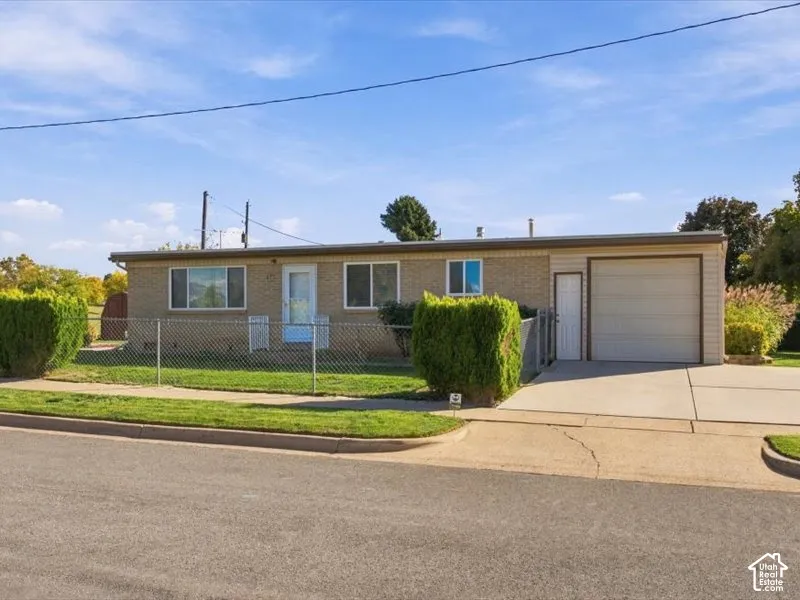 Single-story brick exterior featuring an attached one-car garage, concrete driveway, and chain-link perimeter fencing