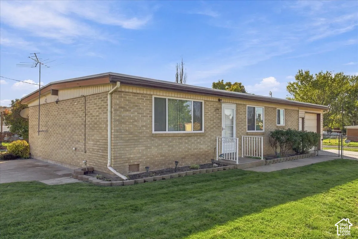 Single-story brick exterior featuring a low-pitch roofline, attached one-car garage, concrete driveway, and front landscape with stone edging