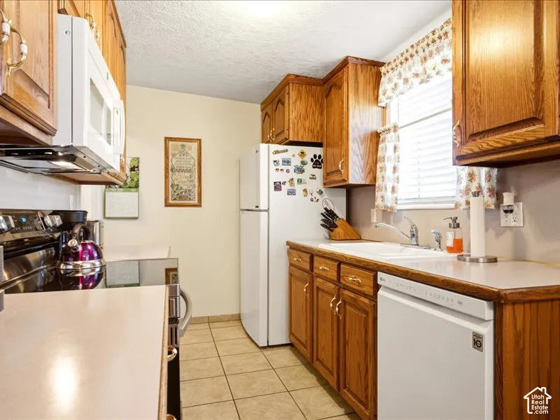 Kitchen featuring wood cabinetry, white appliances, solid-surface countertops, dual-basin sink, and tile flooring