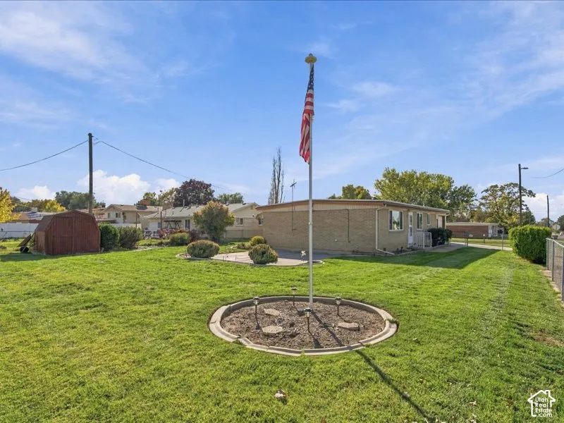 Expansive lawn featuring a concrete patio, detached shed, and a circular landscaped planter with a central flagpole
