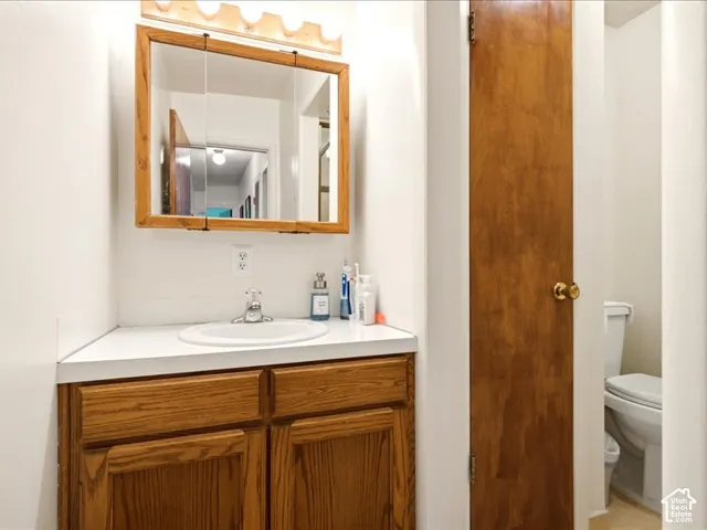 Wood-finish cabinetry, solid-surface countertop with an integrated basin, tri-fold medicine cabinet, and wall-mounted vanity lighting