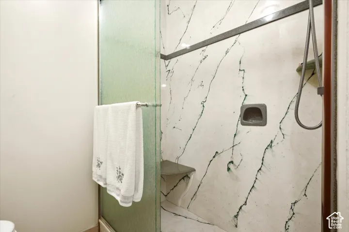 Walk-in shower featuring patterned wall surround, integrated corner bench, built-in recessed shelf, and frosted glass enclosure with metal hardware