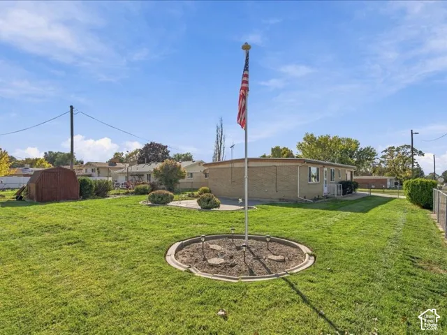 Expansive lawn featuring a concrete patio, detached shed, and a circular landscaped planter with a central flagpole