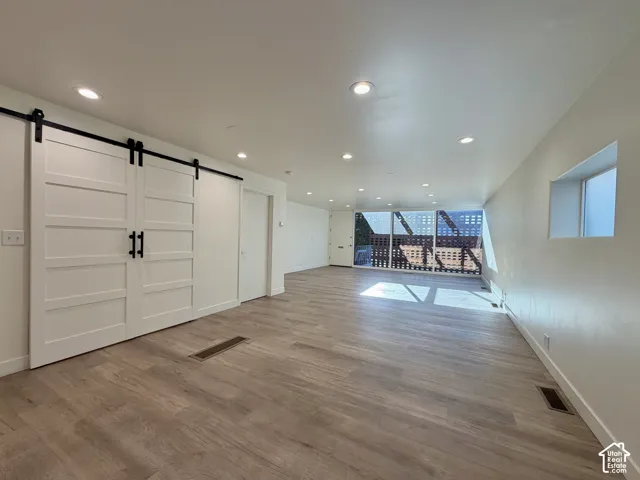 Interior space featuring wood-finish flooring, white double sliding barn doors with matte black hardware, recessed lighting, and expansive floor-to-ceiling windows