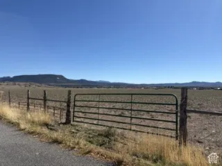Expansive open acreage featuring a metal tubular gate, post-and-wire fencing, and a mountain backdrop