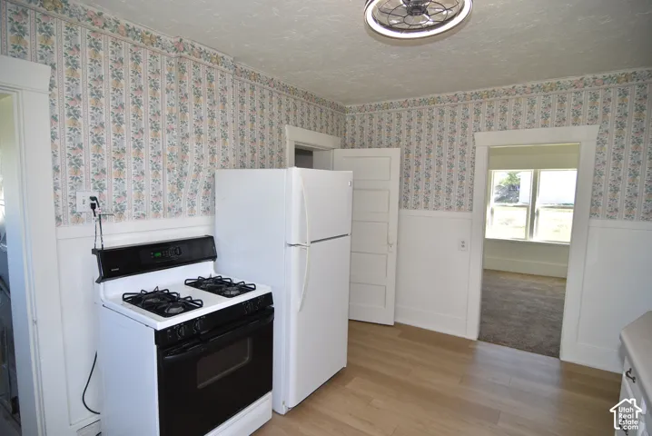 Kitchen featuring wood-finish flooring, half-wall wainscoting, white appliances, and five-panel interior doors