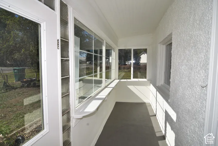 Enclosed porch featuring large picture windows, vertical glass block accents, painted concrete flooring, textured wall finishes, and a beadboard ceiling