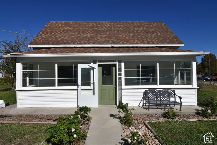 Exterior facade featuring white horizontal siding, an enclosed front porch with multi-pane windows, a peaked roof with composite shingles, and a central entryway with a solid-panel door