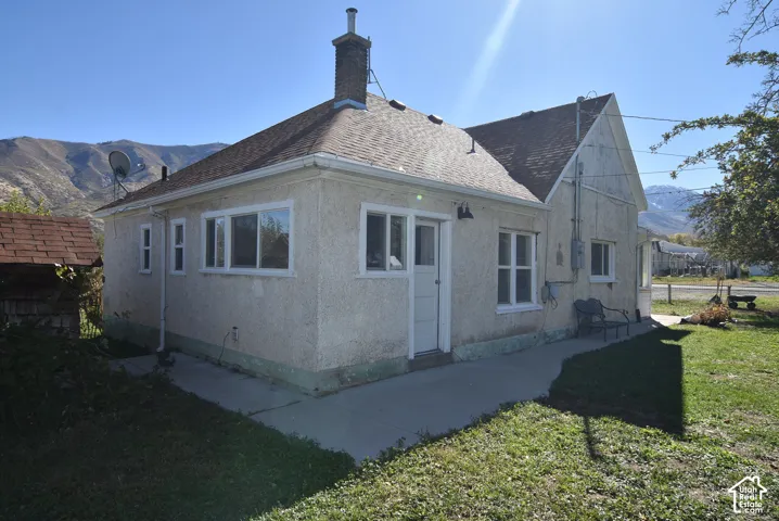 Stucco exterior featuring a shingle roof, chimney, concrete walkway, and mountain backdrop