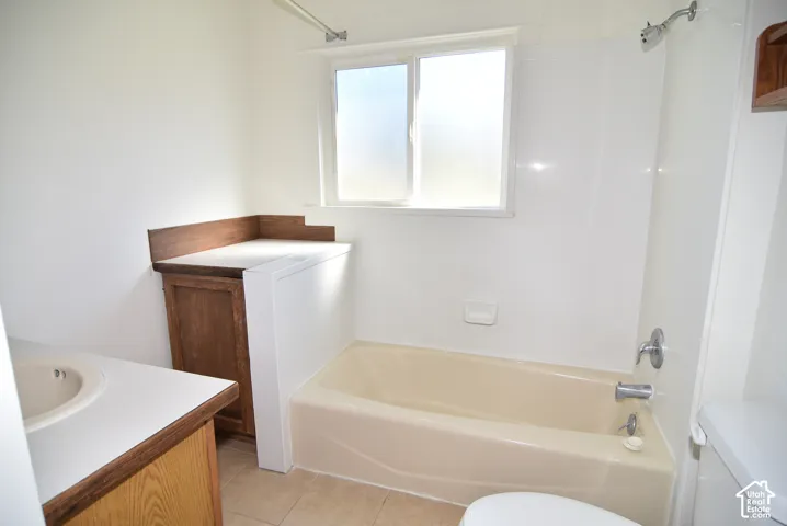 Bathroom featuring a wood-finish vanity with a solid-surface countertop, integrated basin, tub-shower combination with surround, and tile flooring