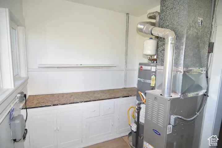 Utility area featuring a built-in cabinet base with stone-finish countertop, white upper wall shelf, and installed water heating and HVAC systems