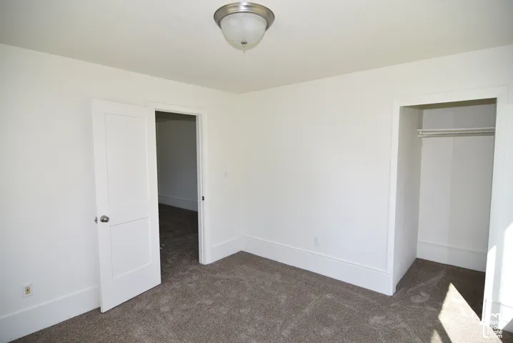 Neutral-toned wall-to-wall carpeting, white interior walls, flush-mount ceiling light fixture, and walk-in closet with built-in shelving