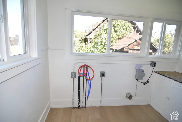 Utility area featuring wood-finish flooring, white cabinetry, expansive windows, and dedicated plumbing and electrical hookups