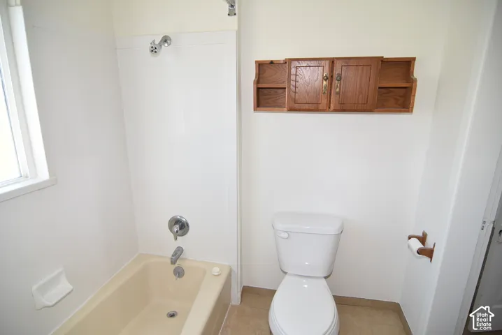 Bathroom featuring a tub with a surround, wall-mounted shower faucet, dual-flush toilet, and built-in wood-finish wall cabinetry