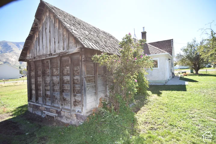 Exterior structure featuring a weathered wood-plank facade, pitched roof, and a stone foundation, set upon a lawn with a mountain backdrop