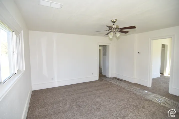 Neutral-toned interior space featuring wall-to-wall carpeting, white walls, and a ceiling-mounted light fixture with a fan