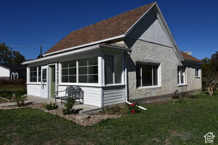 Exterior featuring a textured stucco facade, a multi-pane enclosed porch, and a shingled gable roof