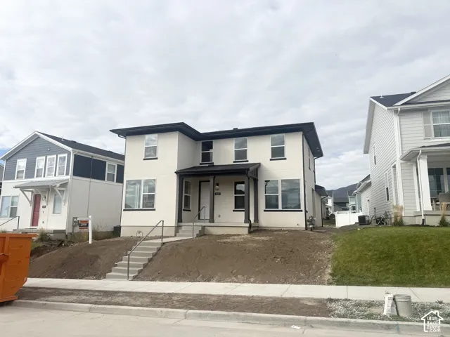 Two-story exterior featuring a light-toned smooth facade, dark-trimmed rectangular windows, a covered front entryway, and concrete steps with metal handrails