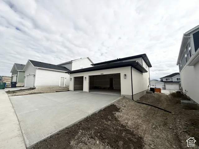 Two-car garage with concrete driveway, light-colored stucco exterior, and black metal gutters