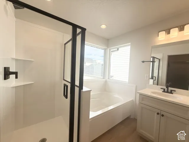 Walk-in shower with black-framed glass enclosure, soaking tub, vanity with solid surface countertop, matte black fixtures, and recessed lighting