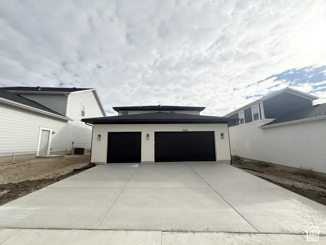 Two-car garage exterior featuring a concrete driveway, smooth light-toned siding, dark-finish garage doors, and three exterior wall-mounted light fixtures