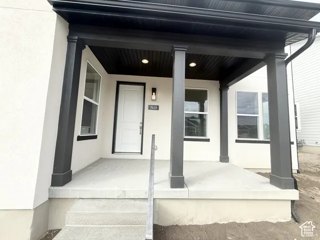 Covered front porch featuring concrete flooring, dark-toned support columns, recessed ceiling lighting, and a modern single-panel exterior door
