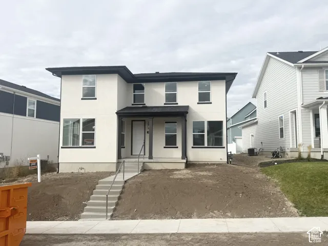 Two-story exterior featuring a light-toned stucco facade, dark trim accents, a covered front entryway, and concrete stairs with metal railing