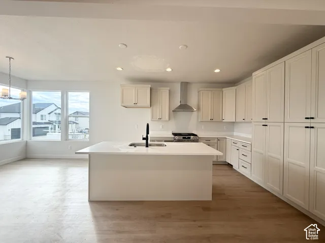 Kitchen featuring light-toned cabinetry, quartz countertops, a central island with an undermount sink, stainless steel range hood, and wood-finish flooring